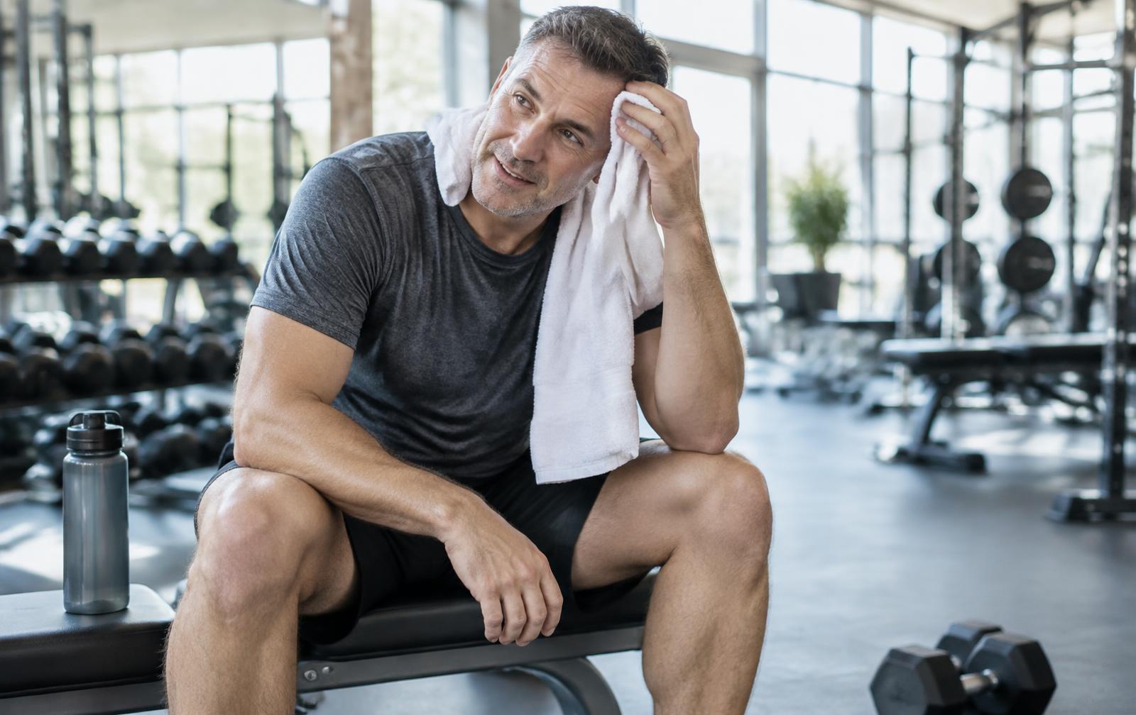 Man in his late 40s resting on a bench after a workout in a bright gym, illustrating questions about whether Sermorelin is a steroid